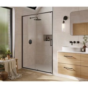 Modern bathroom featuring Merlyn 6 Series Sleek sliding shower door with black frame and frosted glass panel, light wood vanity with white countertop, black wall-mounted faucet, pendant light, rounded mirror, beige tile walls, and natural light from window with green plants