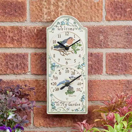 Cream ceramic garden wall clock with robin bird design and integrated thermometer mounted on red brick wall with purple and pink flowers, featuring decorative leaf motifs and "Welcome to My Garden" text