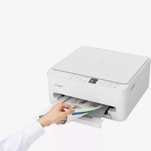 Canon TS6550i white all-in-one wireless inkjet printer with hand pulling out printed color photo from paper tray