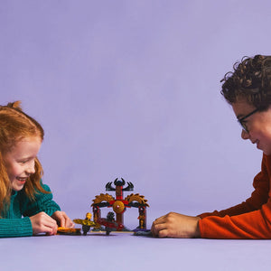 Two children playing with LEGO Dragon Spinjitzu Battle Pack 71826, featuring a red and gold dragon temple set with minifigures on a purple background