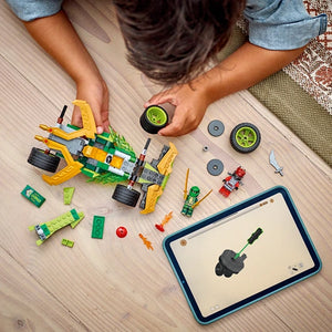 Child assembling green and yellow Lego pull-back race car with wheels and minifigure on wooden floor with instruction tablet and scattered Lego pieces