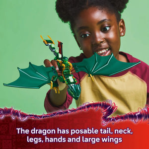 Young child holding green and yellow LEGO dragon toy with posable tail, neck, legs, hands and wings against green background, wearing burgundy and yellow shirt