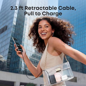 Woman with curly dark hair smiling while holding a black Anker Nano Power Bank with 2.3 ft retractable USB-C cable, wearing a clear crossbody bag against a backdrop of modern glass skyscrapers