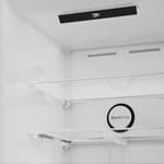 Interior view of Beko anthracite combi fridge freezer showing empty glass shelves, wire racks and round temperature dial on white wall-mounted unit
