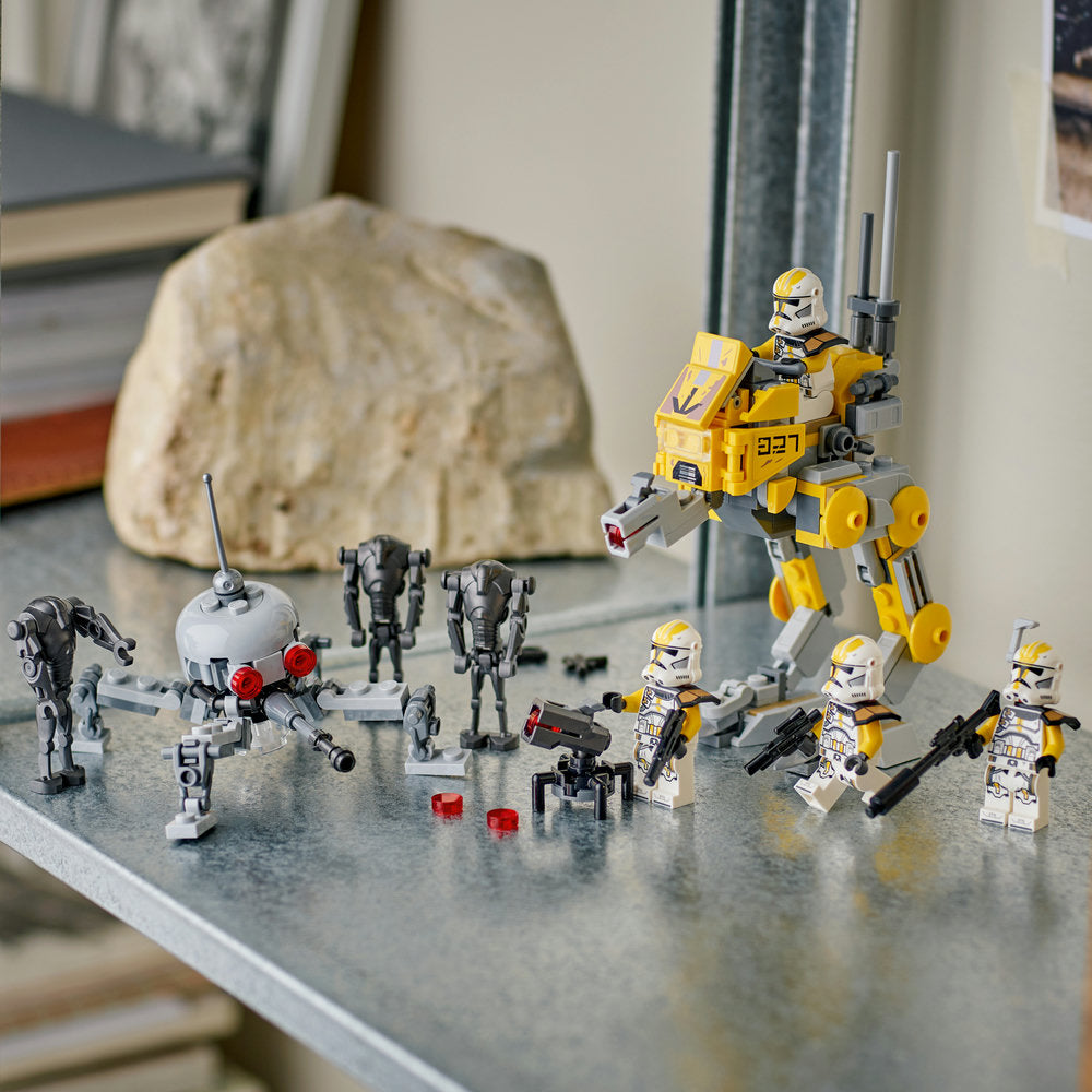 LEGO 327th Star Corps Clone Troopers Battle set 75431 displayed on grey surface featuring yellow and white armored minifigures, gray battle droids, white spherical droid, and yellow mech walker with weapons against blurred indoor background