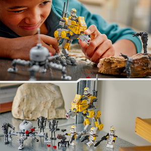 Child playing with LEGO 75431 327th Star Corps Clone Troopers Battle set featuring yellow and black buildable walker vehicle with minifigures, white and grey clone trooper soldiers, and brown rock terrain pieces displayed on grey surface