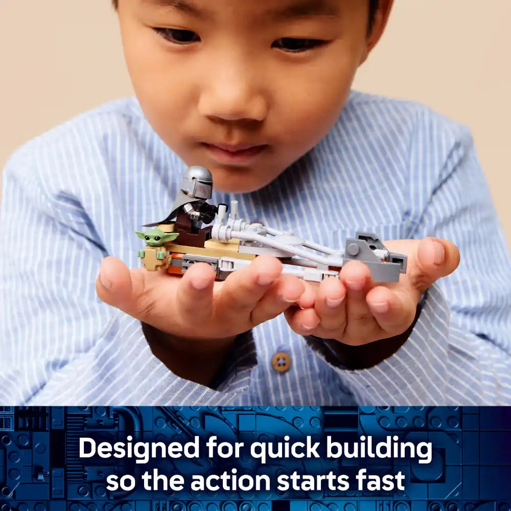 Young child in light blue striped shirt holding assembled LEGO Star Wars Mandalorian speeder bike set featuring minifigures of the Mandalorian and Grogu, displaying the compact buildable spacecraft toy with white and gray pieces against a neutral background