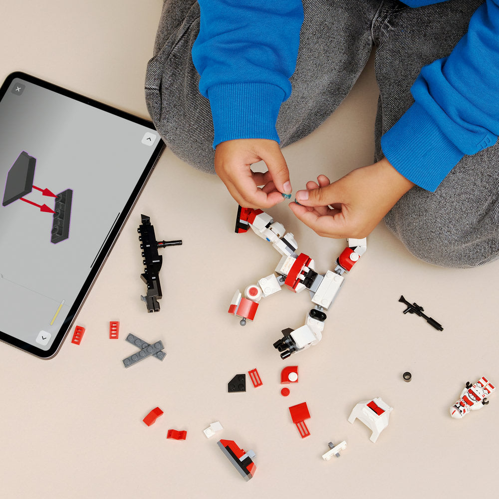 Child's hands assembling red and white LEGO Clone Shock Trooper Mech with instruction manual on tablet, displaying loose bricks and partially constructed figure on beige surface