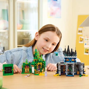 Young child playing with LEGO Wicked Emerald City and Kiamo Ko Castle set featuring green castle with gold accents and black castle tower on wooden table in bright classroom setting