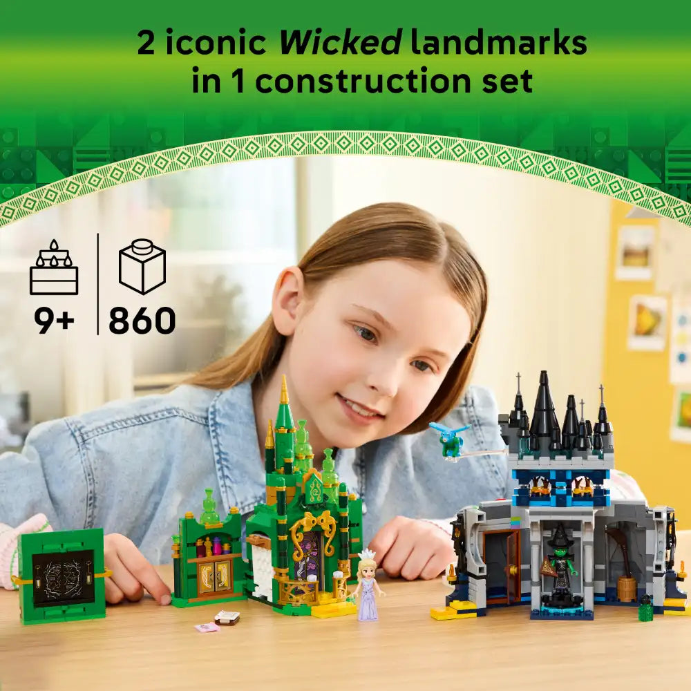 A young girl with reddish-brown hair smiling while playing with two LEGO Wicked construction sets on a wooden table: a green Emerald City castle with golden details and a dark gray Kiamo Ko Castle with black spires, featuring 860 pieces total, recommended for ages 9 and up