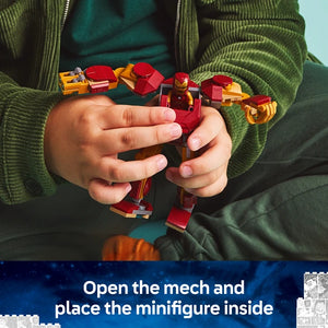 Child's hands holding red and gold LEGO Iron Man mech suit with yellow and red vehicles, wearing green knit cardigan, instructional text below reading Open the mech and place the minifigure inside