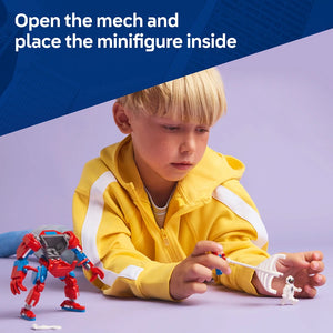 Young child in yellow jacket with white stripes playing with red and blue Lego Spider-Man mech suit, with white Lego minifigure visible on purple background, demonstrating opening mech cockpit to place minifigure inside