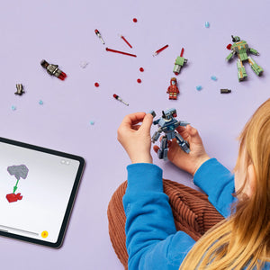 Child's hands holding blue and grey LEGO War Machine minifigure above purple surface with scattered LEGO pieces including red spheres, red lipstick-shaped elements, green and yellow robot, red Iron Man minifigure, and tablet displaying LEGO instructions