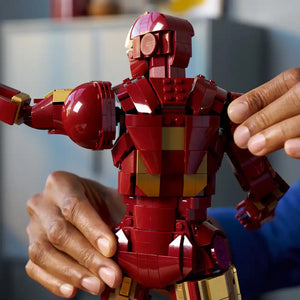 Person holding a red and gold LEGO Iron Man Mark 3 minifigure with articulated limbs and detailed armor plating against a blurred indoor background