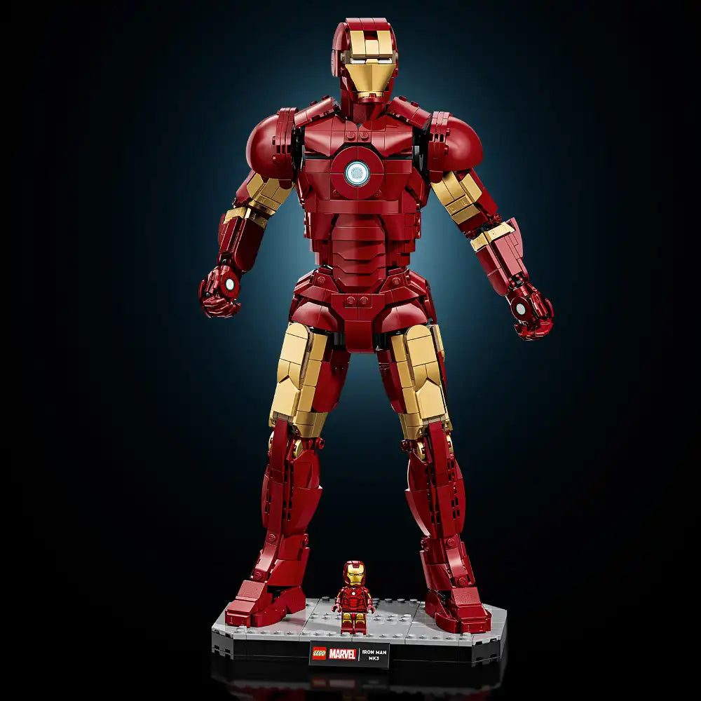 Large LEGO Marvel Iron Man Mark 3 buildable figure in red and gold metallic colors with poseable limbs and glowing chest piece, displayed on gray baseplate with minifigure scale reference, against dark blue gradient background