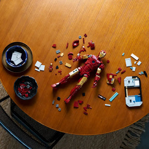 LEGO Iron Man Mark 3 Collector's Edition set 76344 disassembled on wooden table showing red and gold minifigure armor pieces, white instruction manual pages, blue LEGO bricks, and individual components organized in black bowls