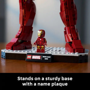 LEGO Marvel Iron Man MK3 minifigure in red and gold standing on white baseplate with black name plaque, flanked by two large red armor leg pieces, displayed on wooden surface