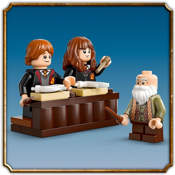 LEGO minifigures depicting a Hogwarts Charms Class scene with two students in black robes at a wooden desk with books and a wand, and an elderly wizard with white beard in green robes standing beside them, displayed against a blue background in a gold-trimmed frame