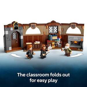 LEGO Hogwarts Castle Charms Class 76442 playset showing a brown and grey stone castle classroom structure with wooden doors and arched windows, featuring three minifigures in black wizard robes and an elderly wizard character, with the text "The classroom folds out for easy play" displayed below
