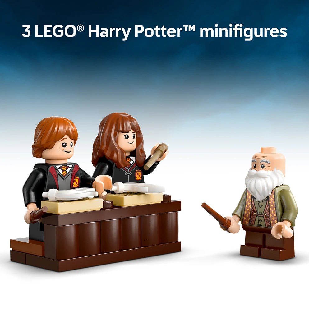 Three LEGO Harry Potter minifigures displayed against a blue gradient background featuring two students with reddish-brown hair in black Hogwarts robes with red and gold trim standing at a brown wooden desk with books and scrolls, and an elderly wizard with a white beard wearing olive green robes with a patterned vest holding a wand