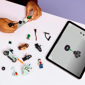 Flat lay product photography of LEGO set 76459 showing disassembled minifigures, vehicles and accessories including a motorcycle, flying car, character figures and green plant pieces, with a tablet displaying an augmented reality view of a purple wheel component on the right side, hands assembling pieces at the top against a white surface with purple background