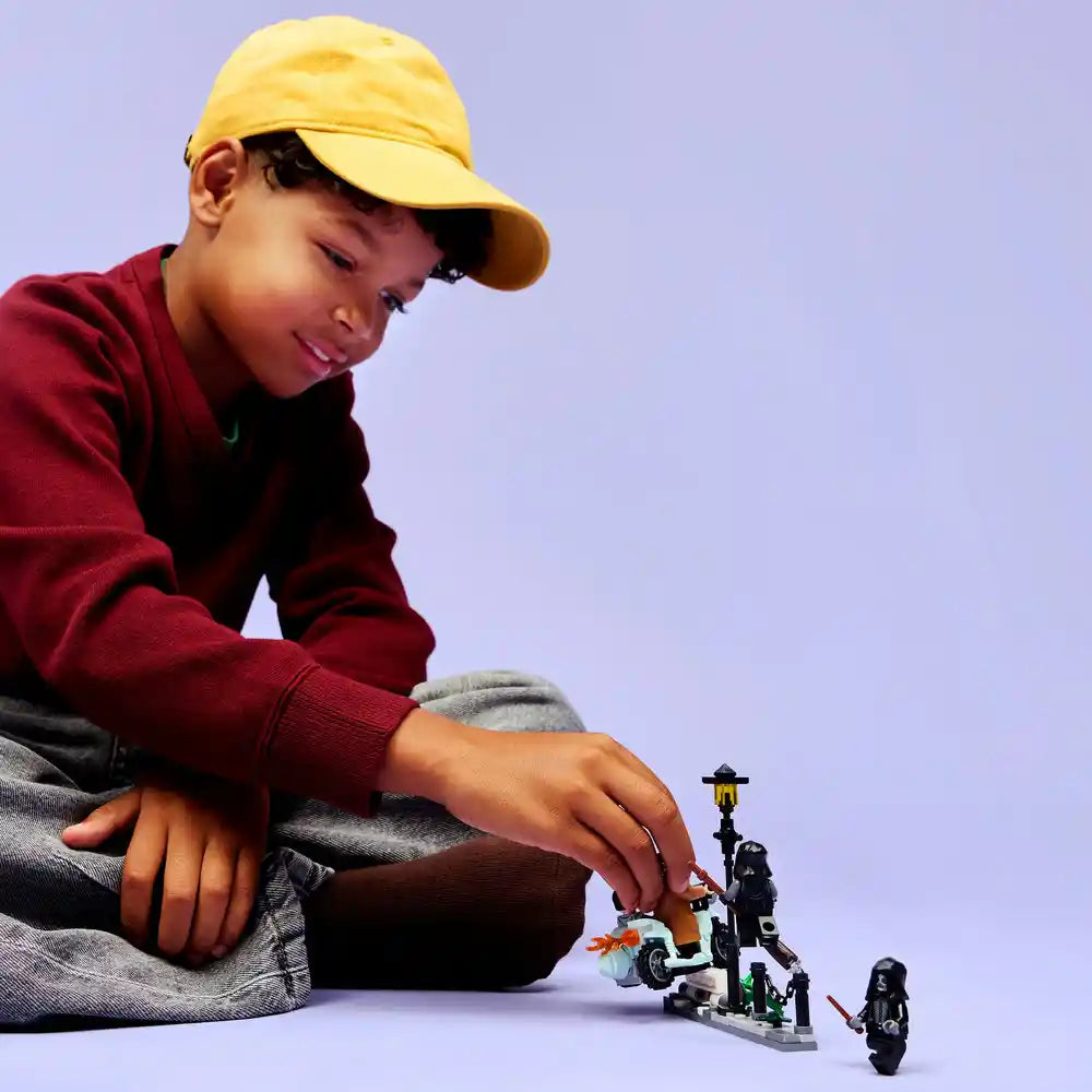 Young child wearing yellow cap and maroon sweater playing with LEGO Harry Potter set 76459 featuring Hagrid and Harry's Privet Drive Escape motorcycle and minifigures against purple background
