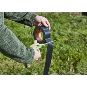 Child's hands holding black Gorilla Tape roll being unrolled outdoors against green garden background, demonstrating the product's durability and width