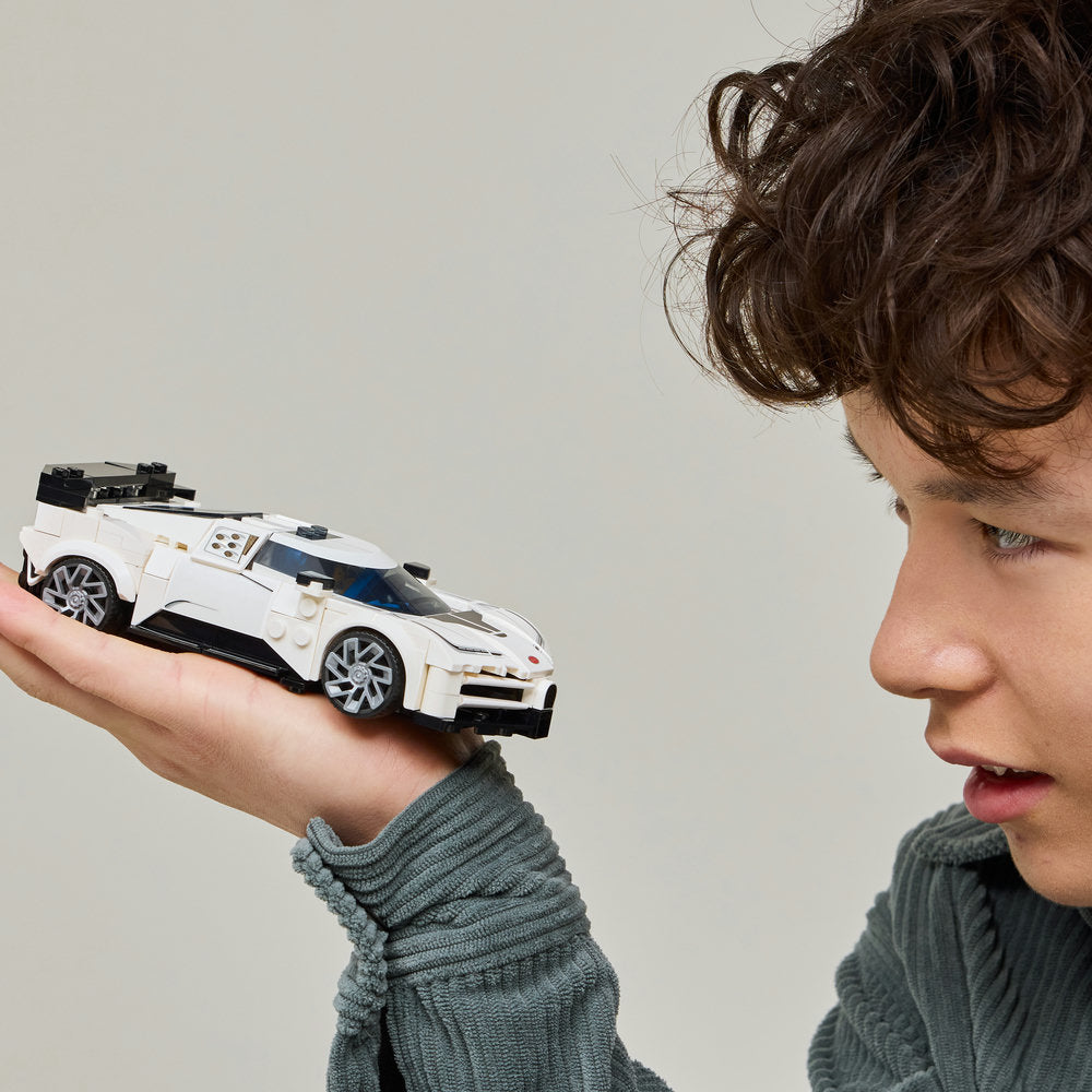 Child holding white and black LEGO Bugatti Centodieci sports car model against neutral background, showcasing detailed brick construction and silver wheels