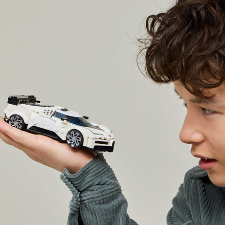 Child holding white and black LEGO Bugatti Centodieci sports car model against neutral background, showcasing detailed brick construction and silver wheels