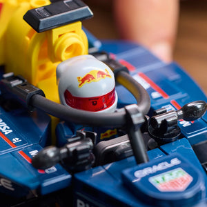 LEGO Oracle Red Bull Racing RB20 F1 race car set featuring a white and red minifigure helmet with Red Bull logo on blue baseplate, yellow pit crane accessory, and detailed black and gray vehicle components