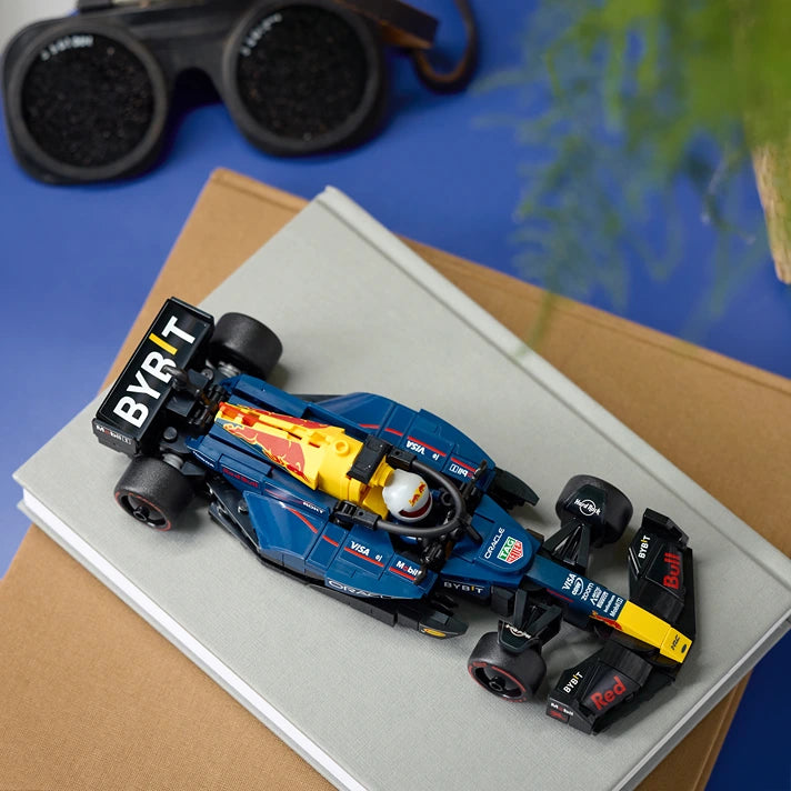 Blue and yellow LEGO Formula 1 race car model with Red Bull Racing branding displayed on white box with binoculars and map visible in background
