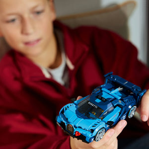 Child in maroon jacket holding bright blue LEGO Bugatti Vision GT sports car model with black accents and detailed features against blurred background