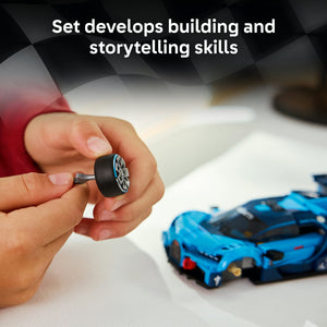 Child's hand holding a black LEGO wheel piece with blue rim details above a blue LEGO Bugatti Vision GT sports car model on white surface, demonstrating building and storytelling skills
