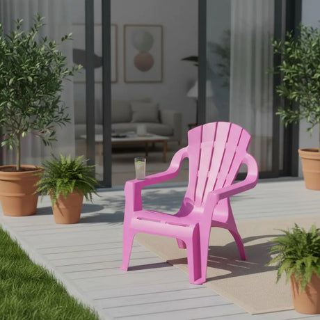 Bright fuchsia pink plastic Adirondack-style children's chair positioned on a light wooden deck surrounded by potted green plants and terracotta planters, with a modern home interior visible through glass doors in the background