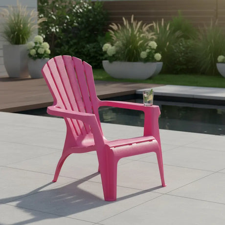 Bright pink Dolomiti Adirondack-style garden chair displayed on a paved patio with a cocktail on the armrest, overlooking a water feature and potted plants with ornamental grasses and white flowers in the background