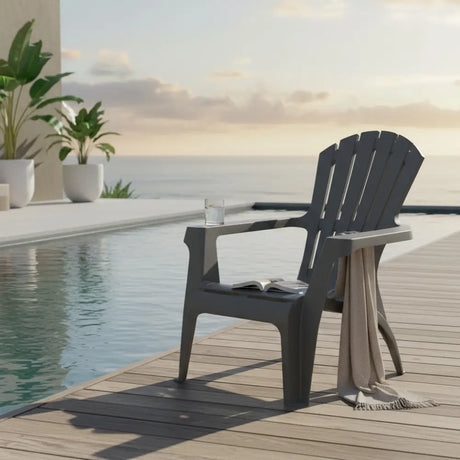 Dolomiti anthracite grey garden chair on wooden deck beside infinity pool with potted plants, glass of water, open book and draped throw blanket overlooking calm sea
