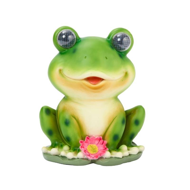 Green smiling frog garden light with bulging eyes, cream belly, pink flower decoration and solar panel eyes on white background