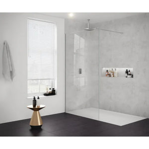 Modern bathroom featuring Merlyn 8mm glass wetroom panel with brushed nickel finish, concrete grey tile walls, black floor tiles, rainfall showerhead, white shower tray, built-in wall niches with toiletries, brass cone side table, white towel rail, and window with horizontal blinds