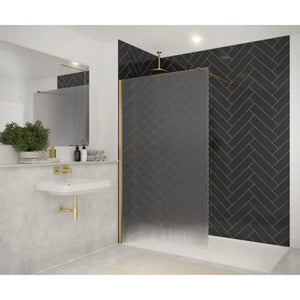 Modern bathroom with Merlyn 8mm wetroom panel featuring textured reeded glass and brushed brass frame, herringbone patterned black tiles on shower wall, white marble-effect tiles, wall-mounted sink with gold fixtures, and contemporary mirror