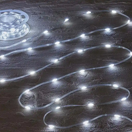 Smart Garden TwoTone rechargeable garden string lights with 200 white and cool LEDs arranged in wavy lines on dark wet ground, showing clear tubing with illuminated bulbs and coiled power unit in top left corner