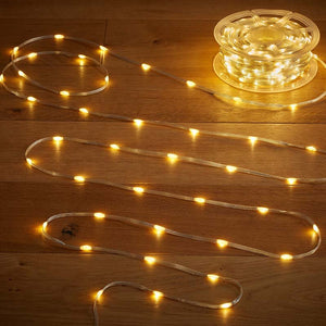Warm white LED string lights with clear tubing displayed on wooden surface showing multiple coiled sections and a transparent spool reel with approximately 200 individual lights