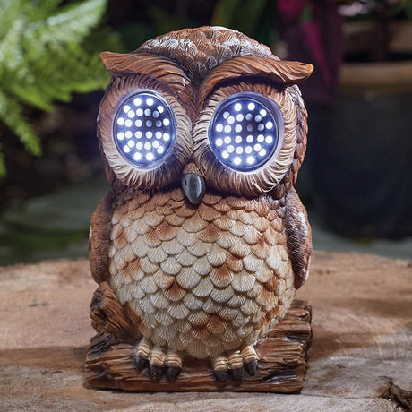 Solar-powered garden owl ornament with carved wooden design, brown and tan feather detailing, illuminated LED eyes glowing blue, perched on wooden base in outdoor garden setting