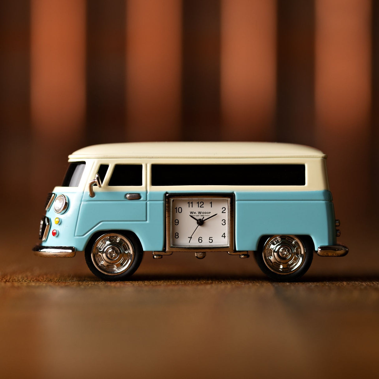 Miniature blue and cream Volkswagen camper van clock with chrome wheels and Widdop branded clock face displaying 10:10 time against brown striped background