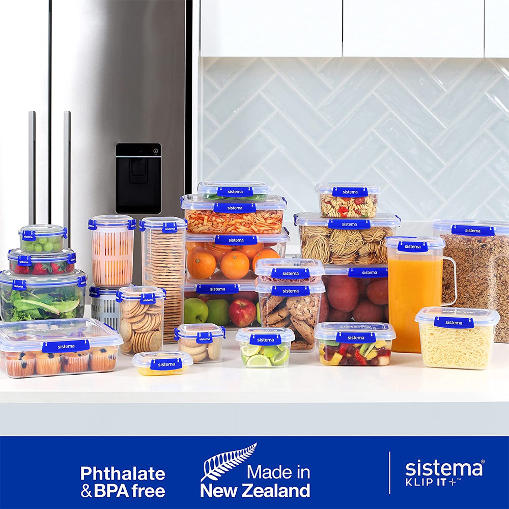 Sistema Klip It Plus food storage containers collection displayed on kitchen counter with fresh produce, pasta, cereals and beverages, featuring blue clip-lock lids, clear plastic bodies, stainless steel refrigerator and herringbone tile backsplash, phthalate and BPA free, made in New Zealand