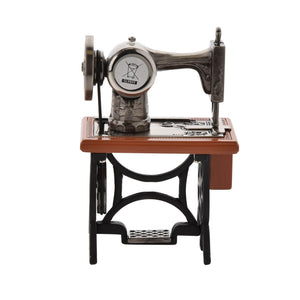 Vintage-style miniature sewing machine clock with cast metal body, wooden base and stand, featuring decorative wheel mechanisms and circular clock face in the center
