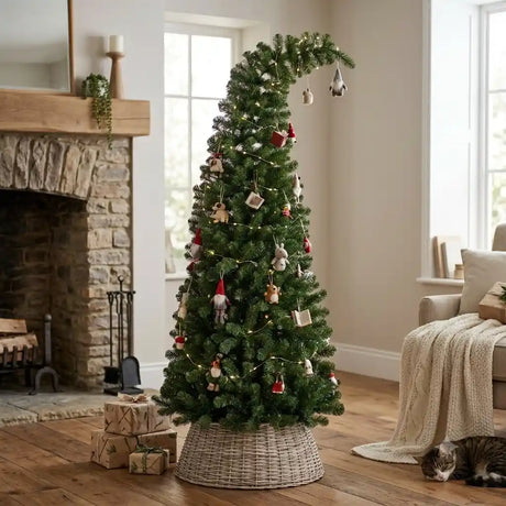 6ft green PVC bendy Christmas tree decorated with wooden and red ornaments, metallic hanging decorations, and warm LED lights in a cozy living room with fireplace, wicker base, wrapped gifts, and cream furnishings