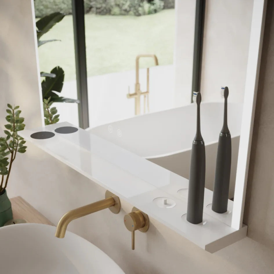 Modern minimalist bathroom with Aqualla Linea Charge LED mirror mounted above white floating vanity, brass wall-mounted faucet, black electric toothbrushes, potted green plant, and large windows overlooking garden