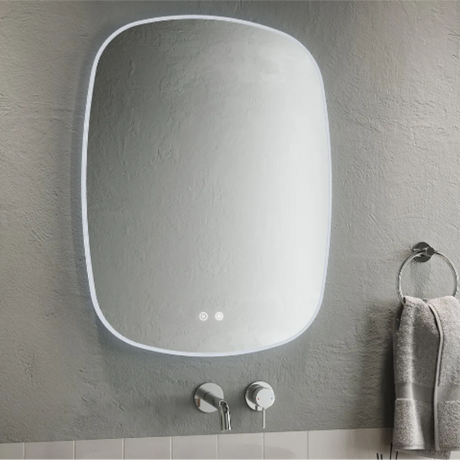 Modern Aqualla Trace LED bathroom mirror with rounded rectangular frame in white, mounted on grey textured wall above white subway tiles, featuring integrated LED lights and chrome wall-mounted faucet with towel ring
