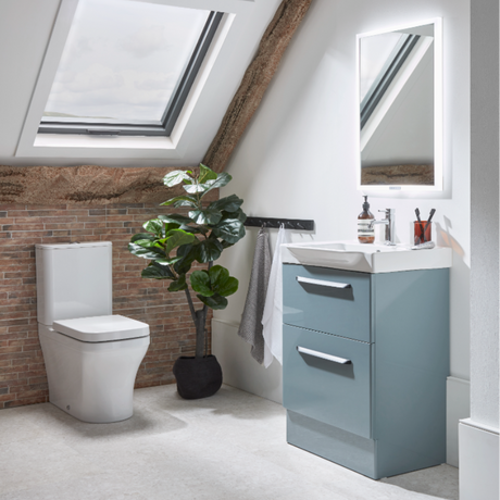 Attic bathroom with Roper Rhodes Academy vanity unit in matt derwent blue featuring white ceramic basin, white toilet, exposed brick wall, skylight windows, wooden beam, potted plant and mirror