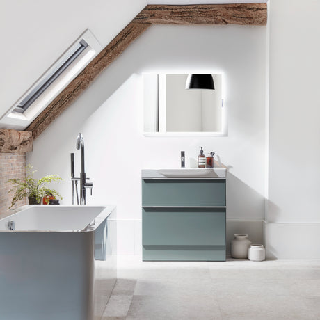 Modern bathroom vanity unit in matt Derwent blue with grey stone countertop and integrated sink, displayed in minimalist attic bathroom with white walls, exposed wooden beams, skylight and illuminated mirror above